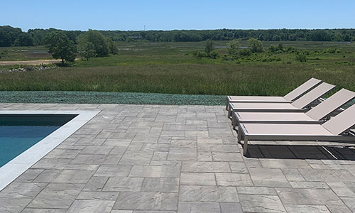 Stone patio with lounge chairs surrounding an inground pool